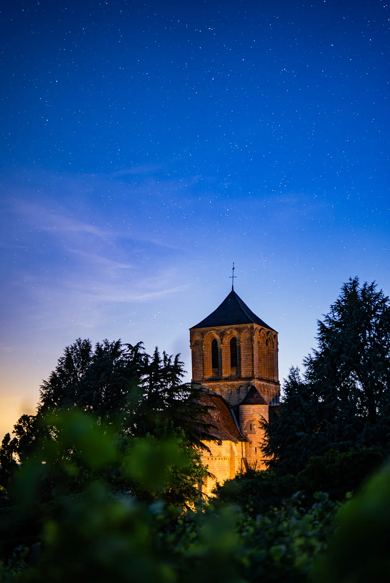 Le clocher de Brion illuminé sous un ciel étoilé, entouré des arbres du domaine