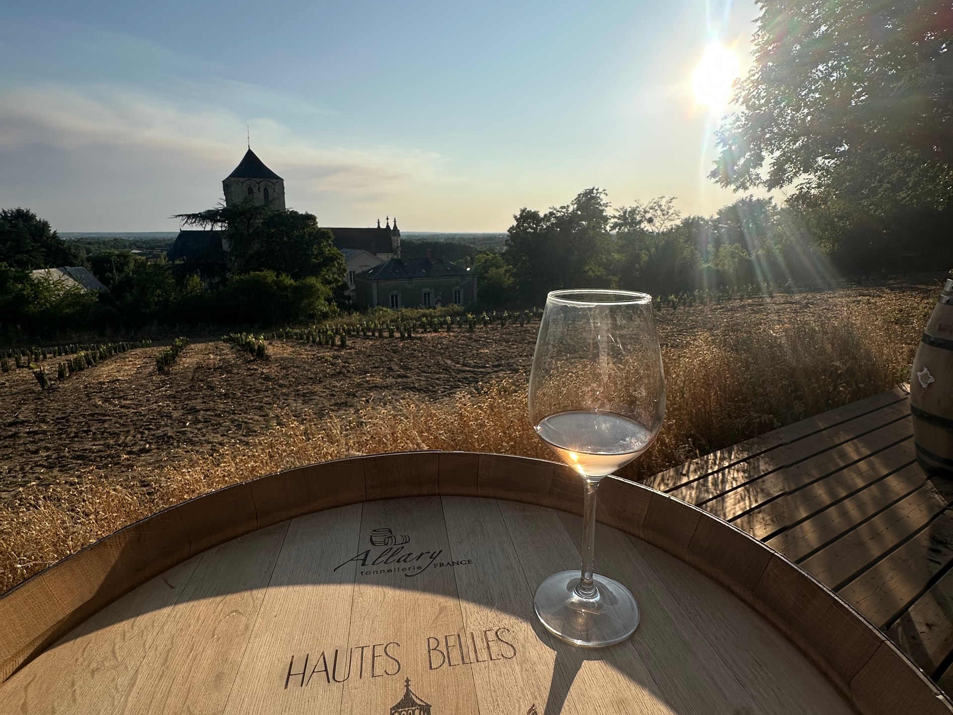 Un verre de vin sur un fût des Hautes Belles, face aux vignes et au clocher de Brion au soleil couchant